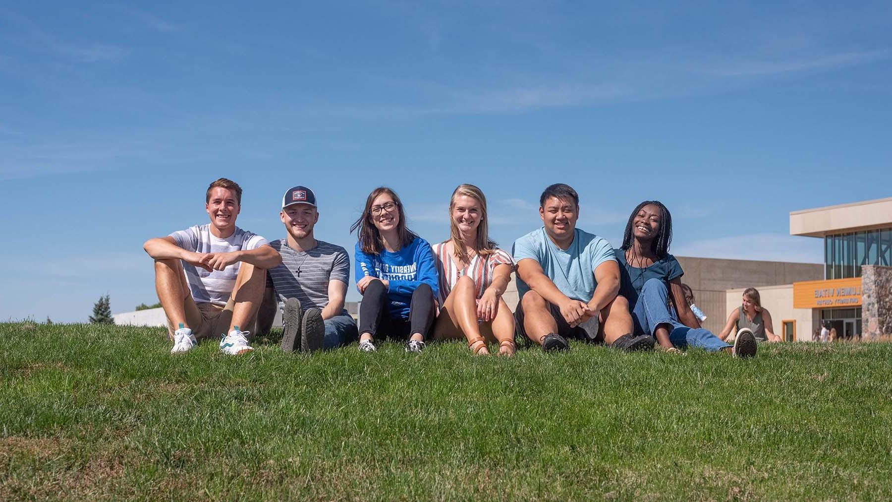 Diverse group of students sitting in grass outside the Lumen Vitae University Center