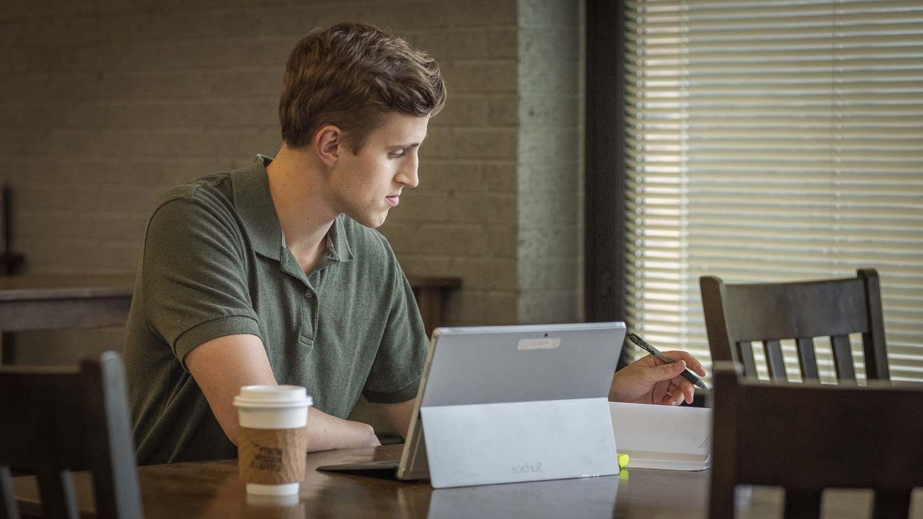 Young man studying with laptop open on table in coffee shop